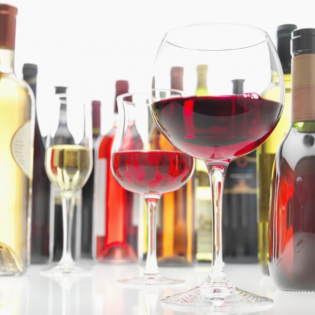 Glasses Of Red And White Wine Encircled By Bottles Of Wines Of Many Kinds, Low View (Focus On Glass Of Red Wine)
