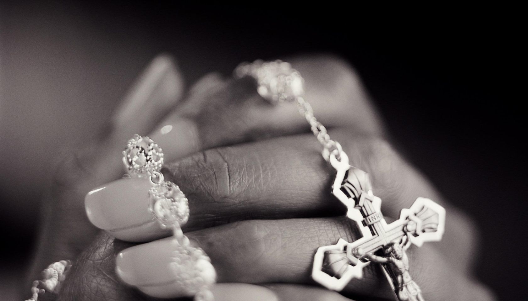 Young woman clasping rosary, close-up (B&W)
