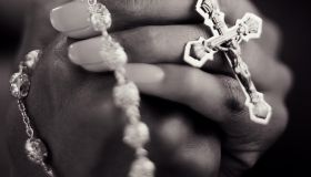 Young woman clasping rosary, close-up (B&W)