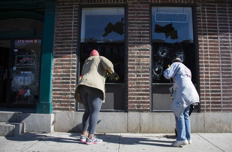 Women take part in recovering Baltimore by cleaning up the front of the local cash checking store.