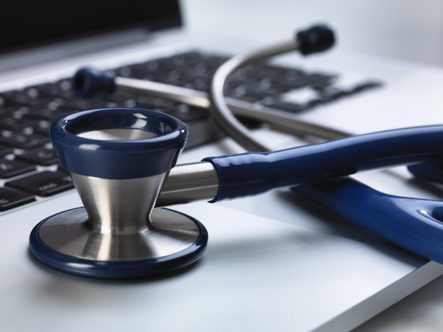 Stethoscope sitting on laptop illustrating online healthcare and doctor's desk
