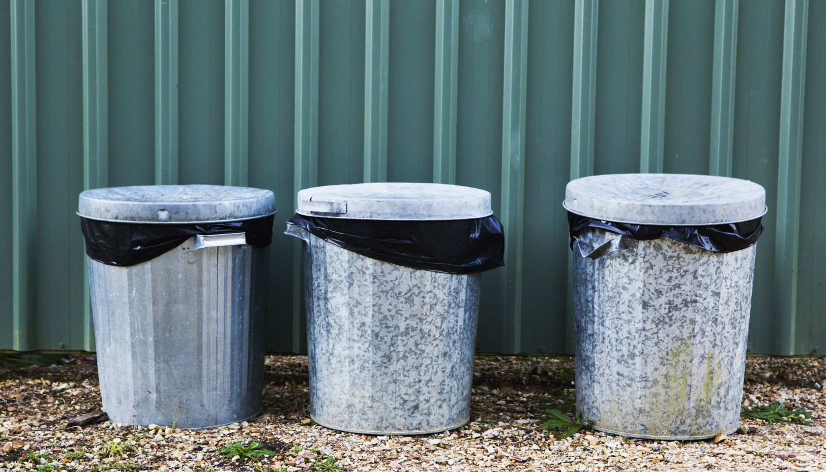Metal Garbage Bins In A Row Against A Metal Wall