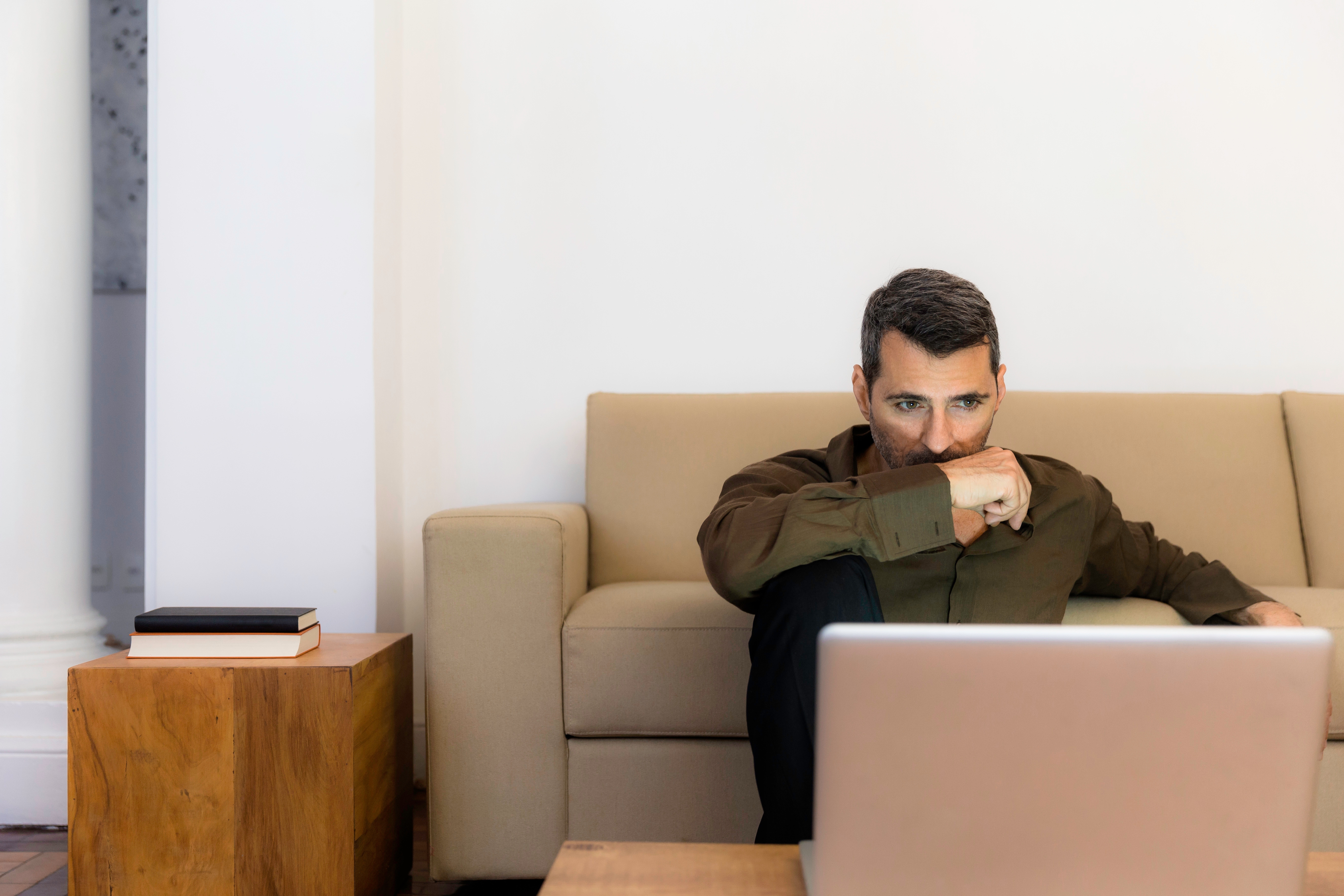 Mature man sitting on floor looking at laptop, arm over mouth