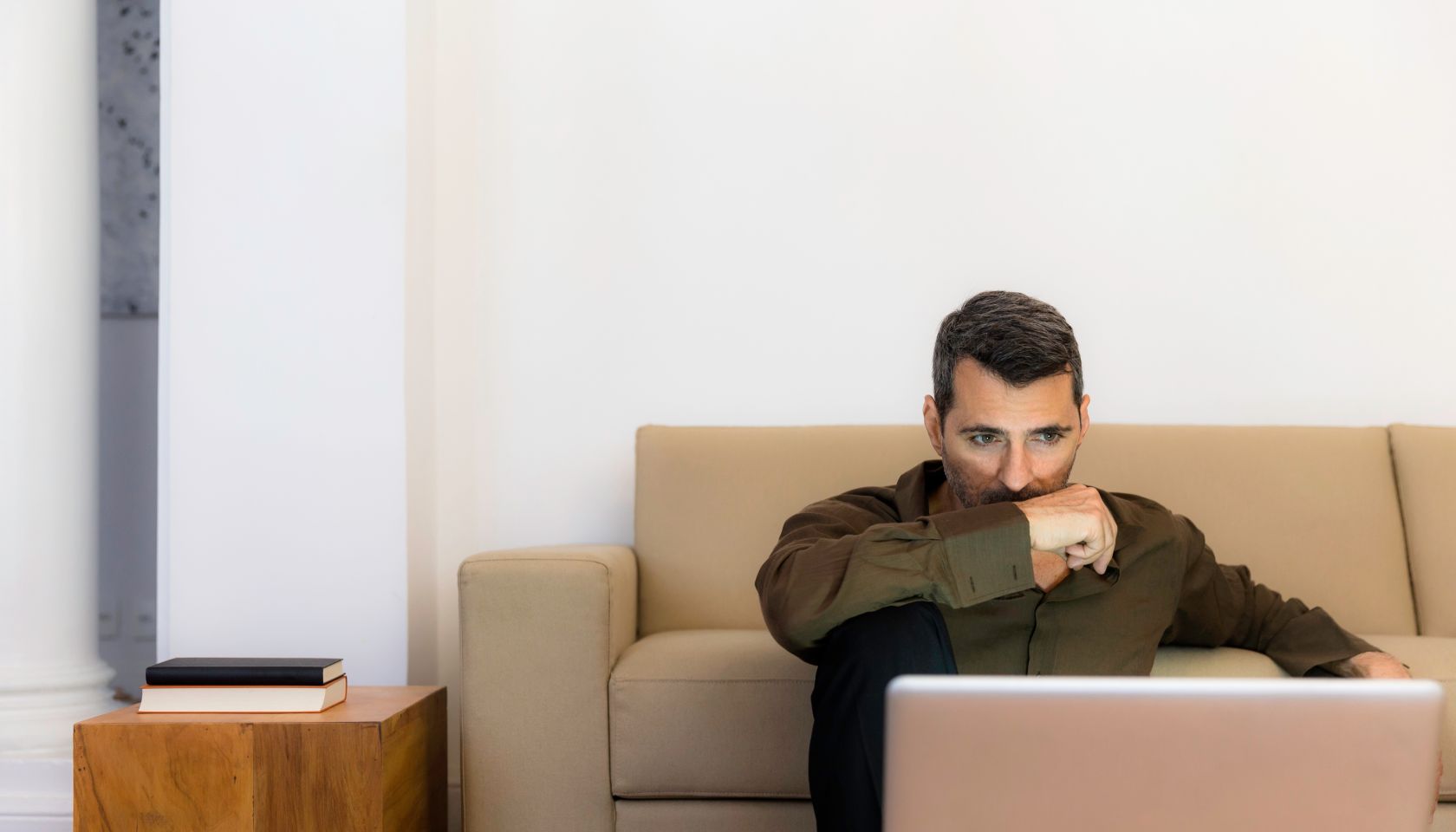 Mature man sitting on floor looking at laptop, arm over mouth