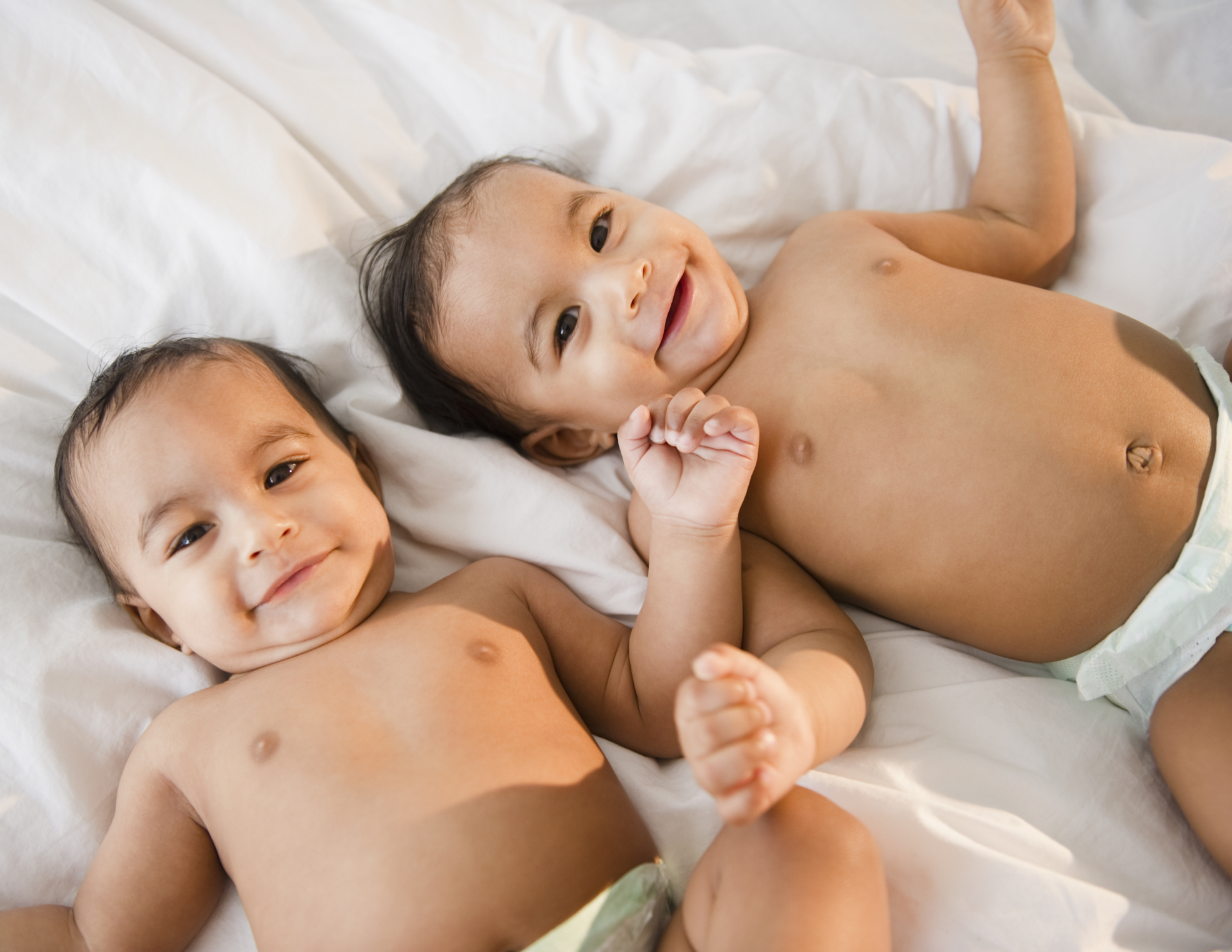 Mixed race twins in diapers laying on bed