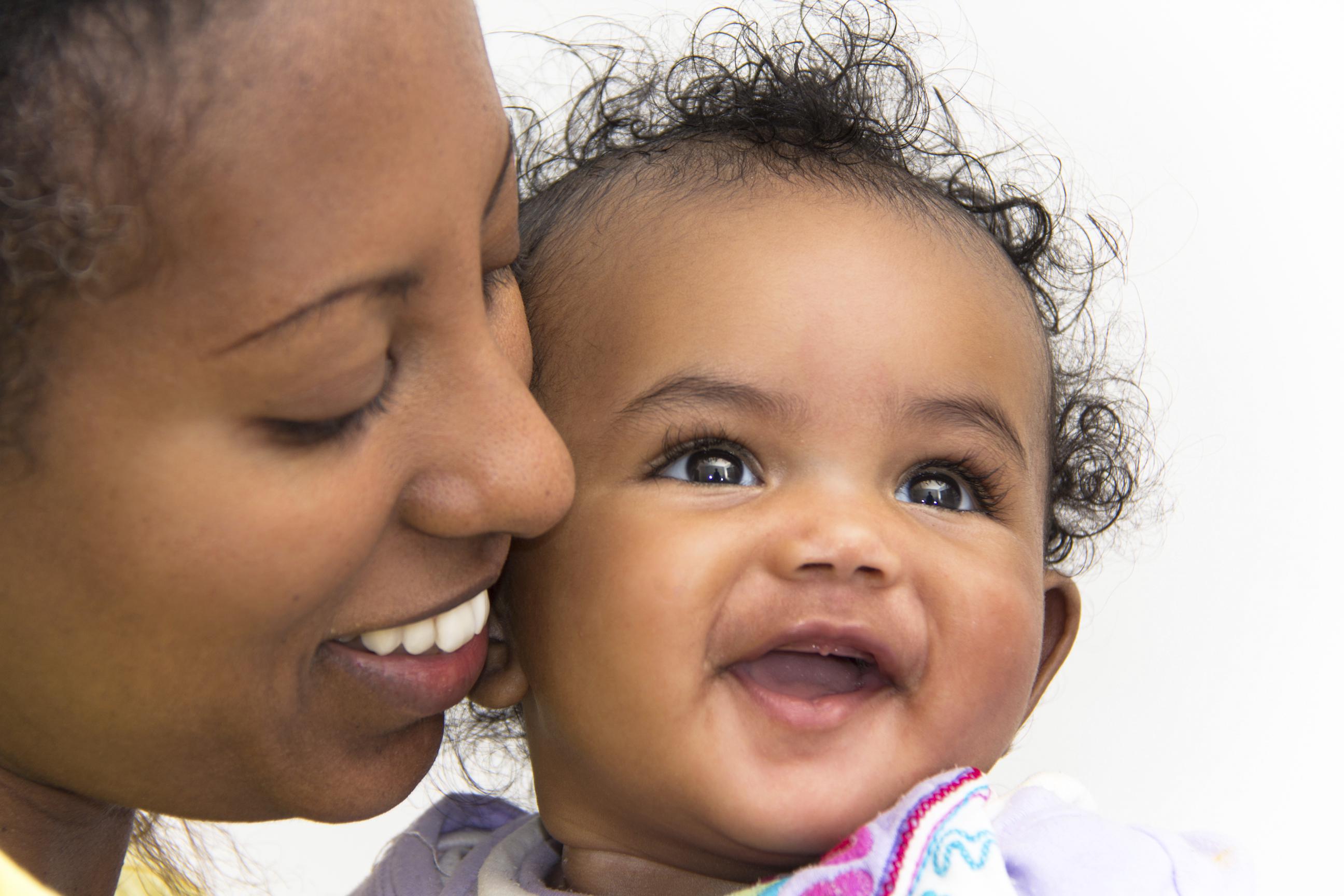 A mother kissing her smiling baby girl on the cheeks