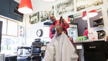 Black barber clipping hair of boy in retro barbershop