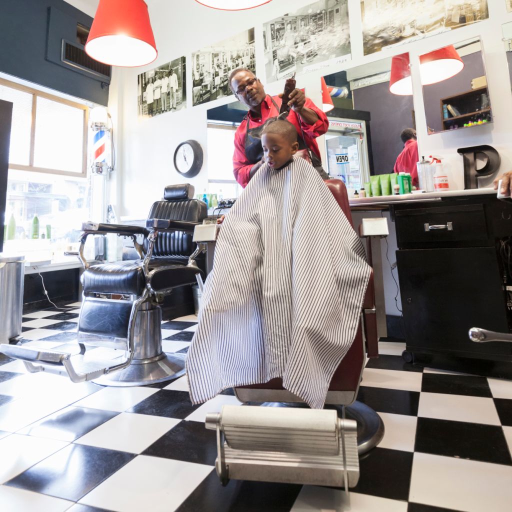 Black barber clipping hair of boy in retro barbershop