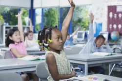 Young children sitting in a classroom at school with their hands raised