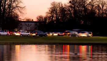 Traffic jam edges slowly forward beside pond dusk