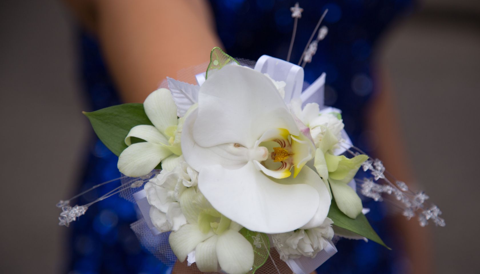 Close up of girl in sparkly blue dress wearing white flower corsage on wrist before prom