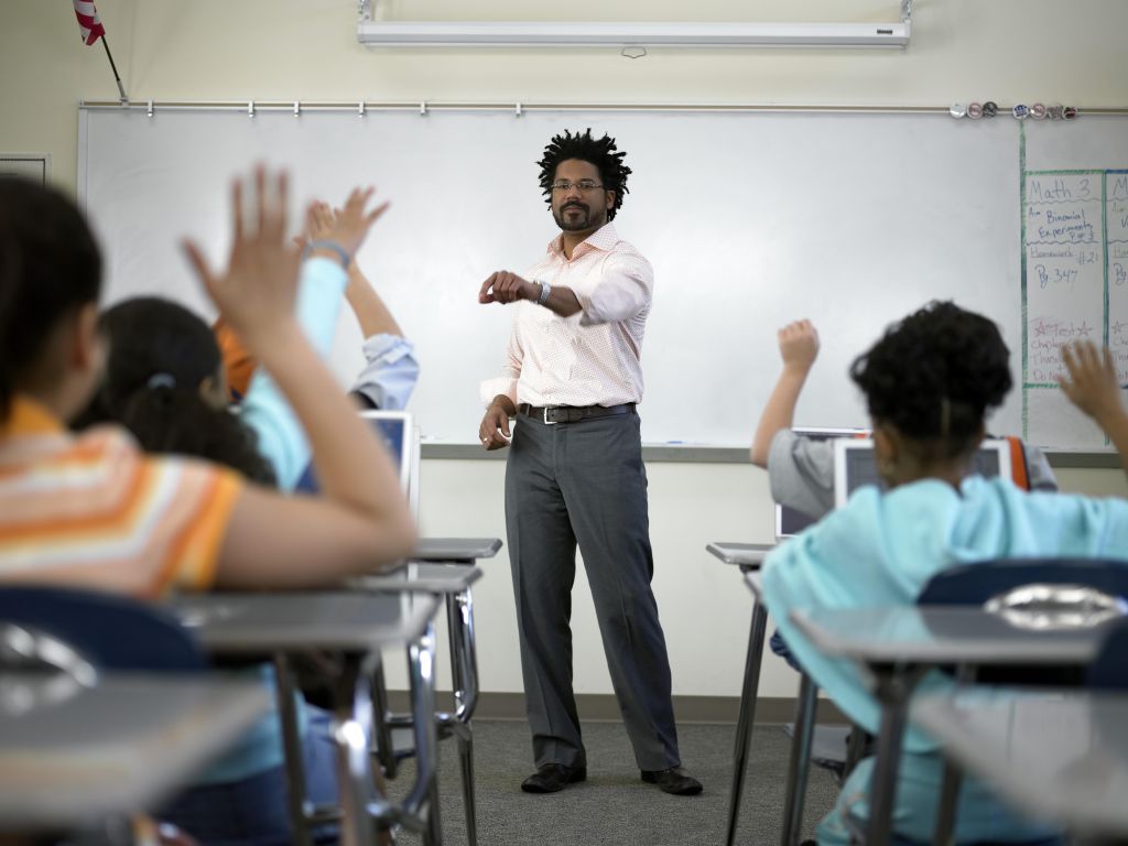 Male teacher standing before students (8-10) with hands raised