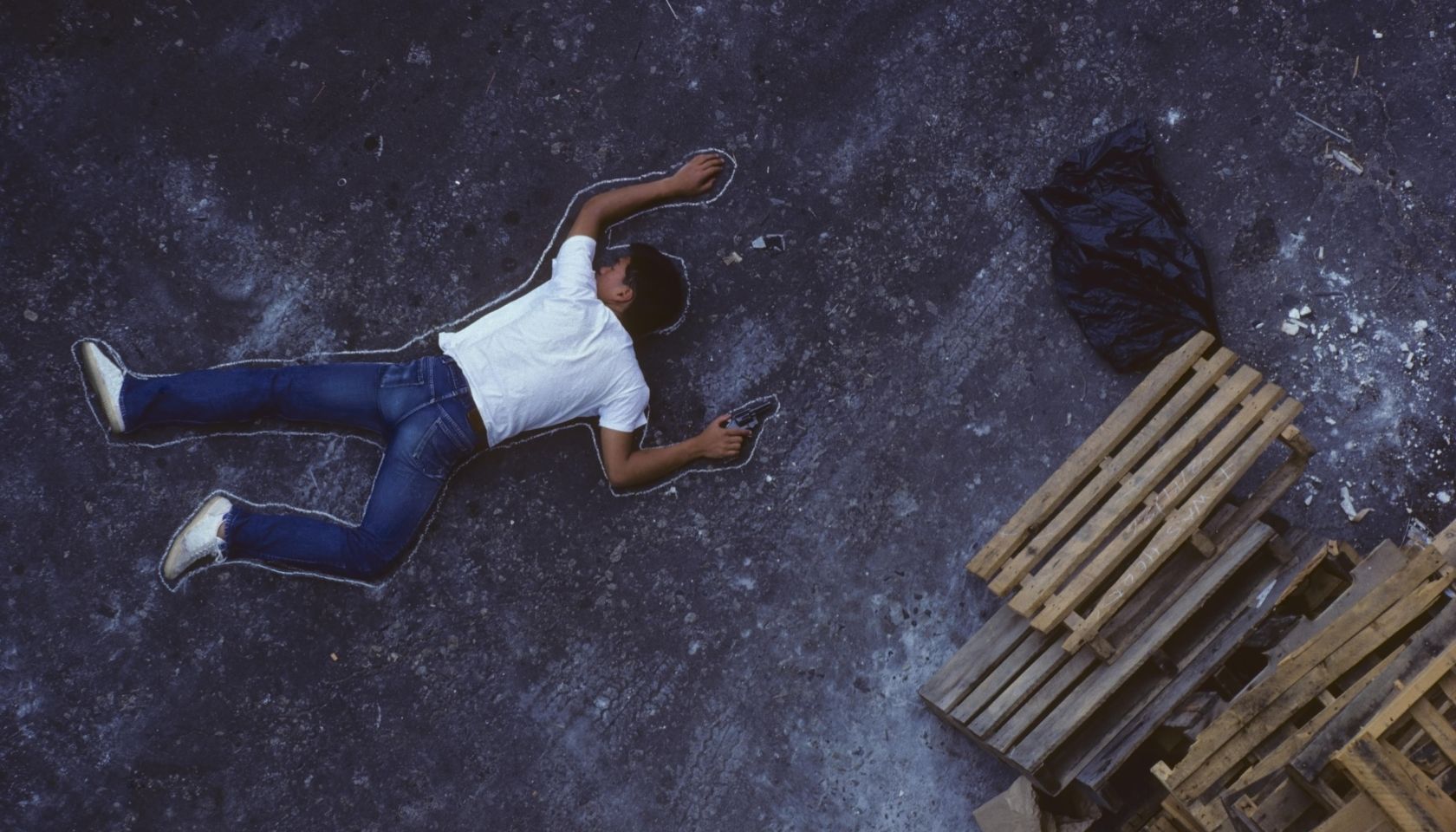 Man with gun lying on ground, chalk outline around him, elevated view