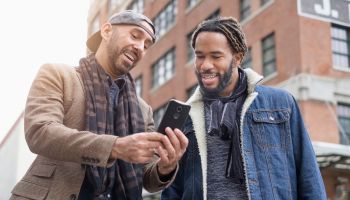 Smiley homosexual couple taking selfie with smart phone in street