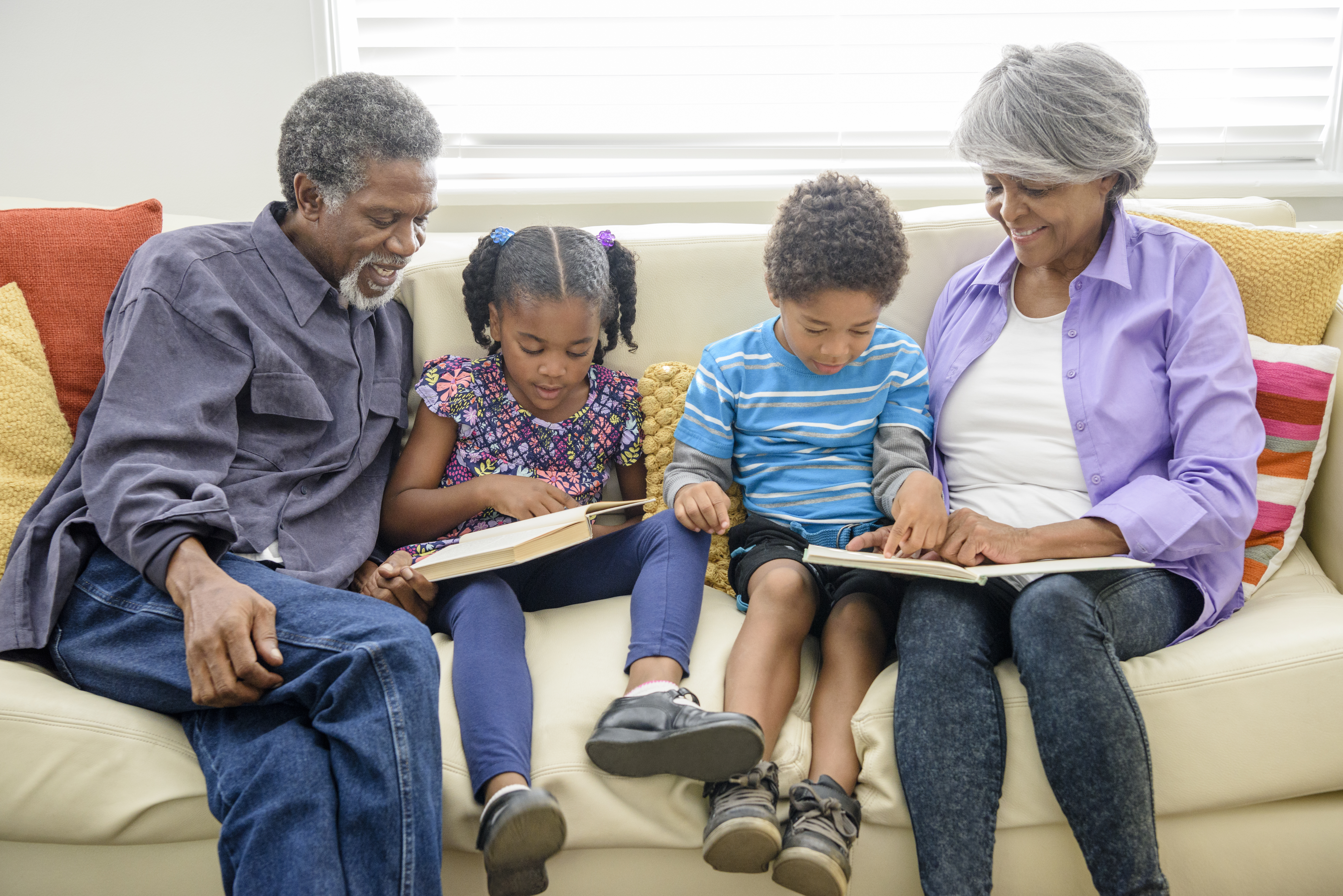 Grandparents sitting on sofa with two grandchildren, reading