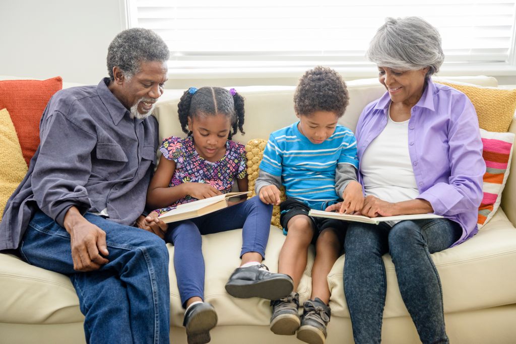 Grandparents sitting on sofa with two grandchildren, reading