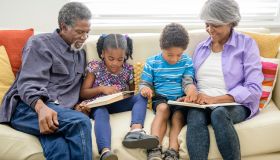 Grandparents sitting on sofa with two grandchildren, reading