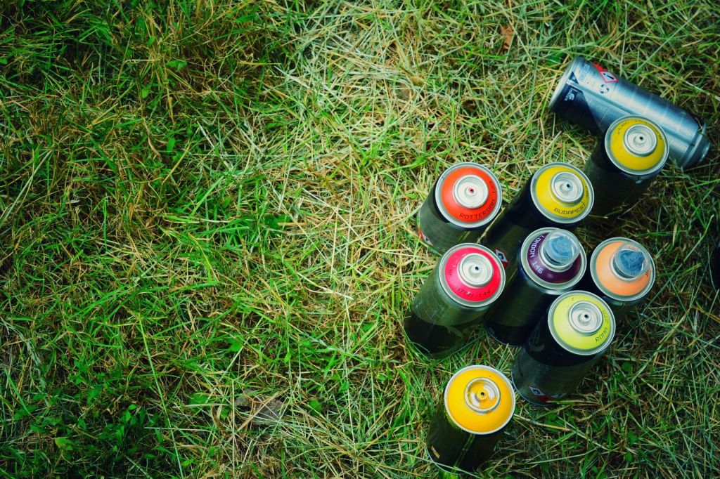 High Angle View Of Colorful Spray Paints On Grassy Field