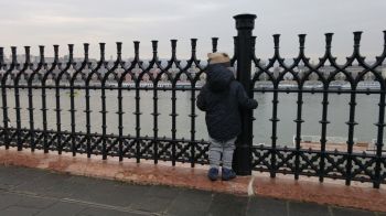 Rear View Of Boy Standing By Fence At Promenade