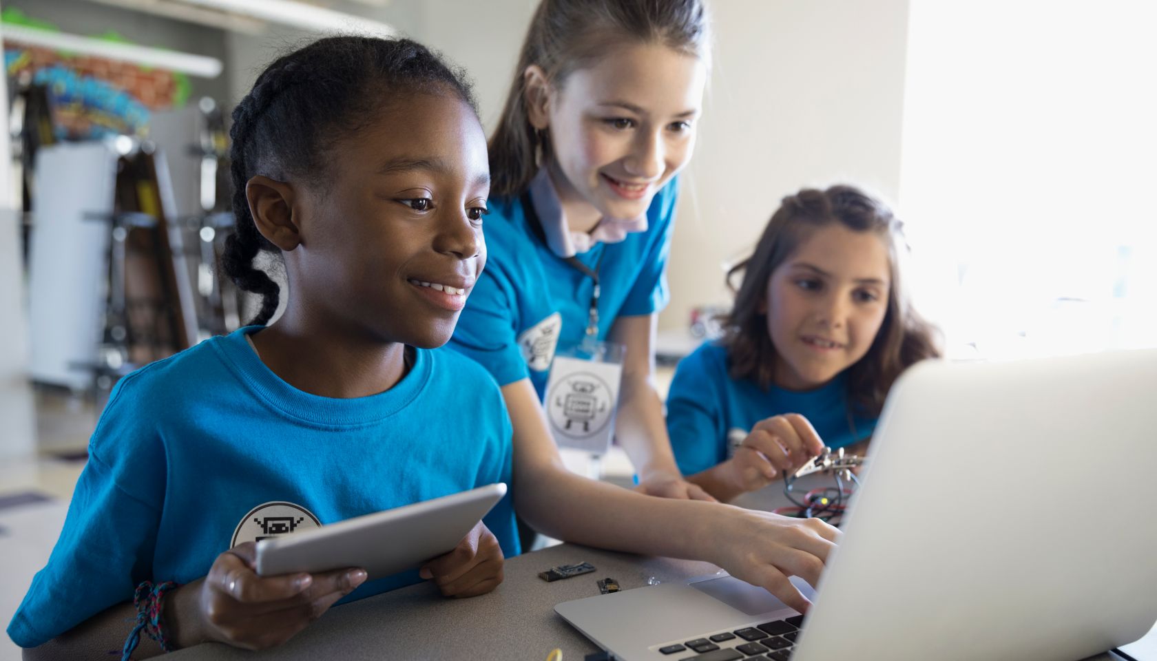 Pre-adolescent girls programming electronics at laptop and digital tablet in classroom
