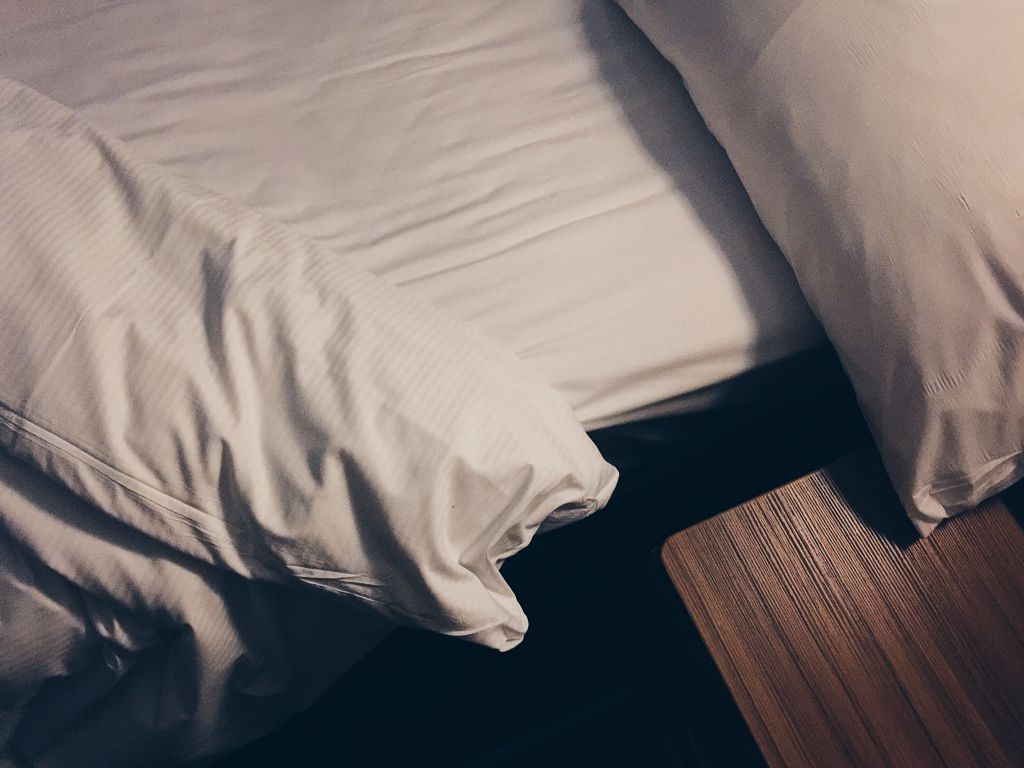 High Angle View Of White Bed By Night Table In Hotel Room