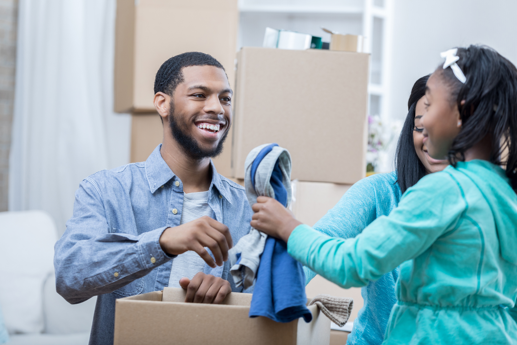 Young family of three packs clothes in moving box together