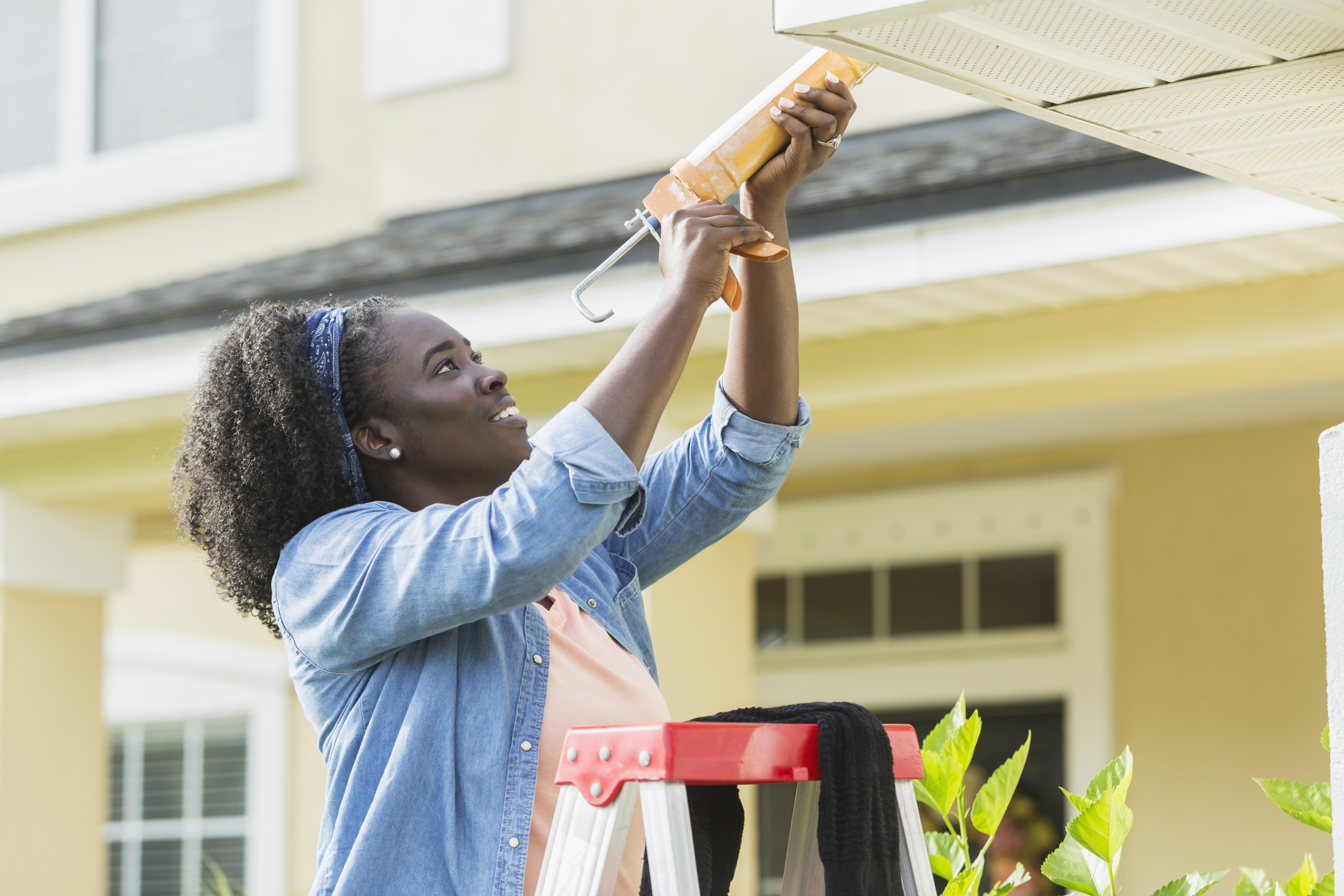 Woman on ladder outside house doing repairs