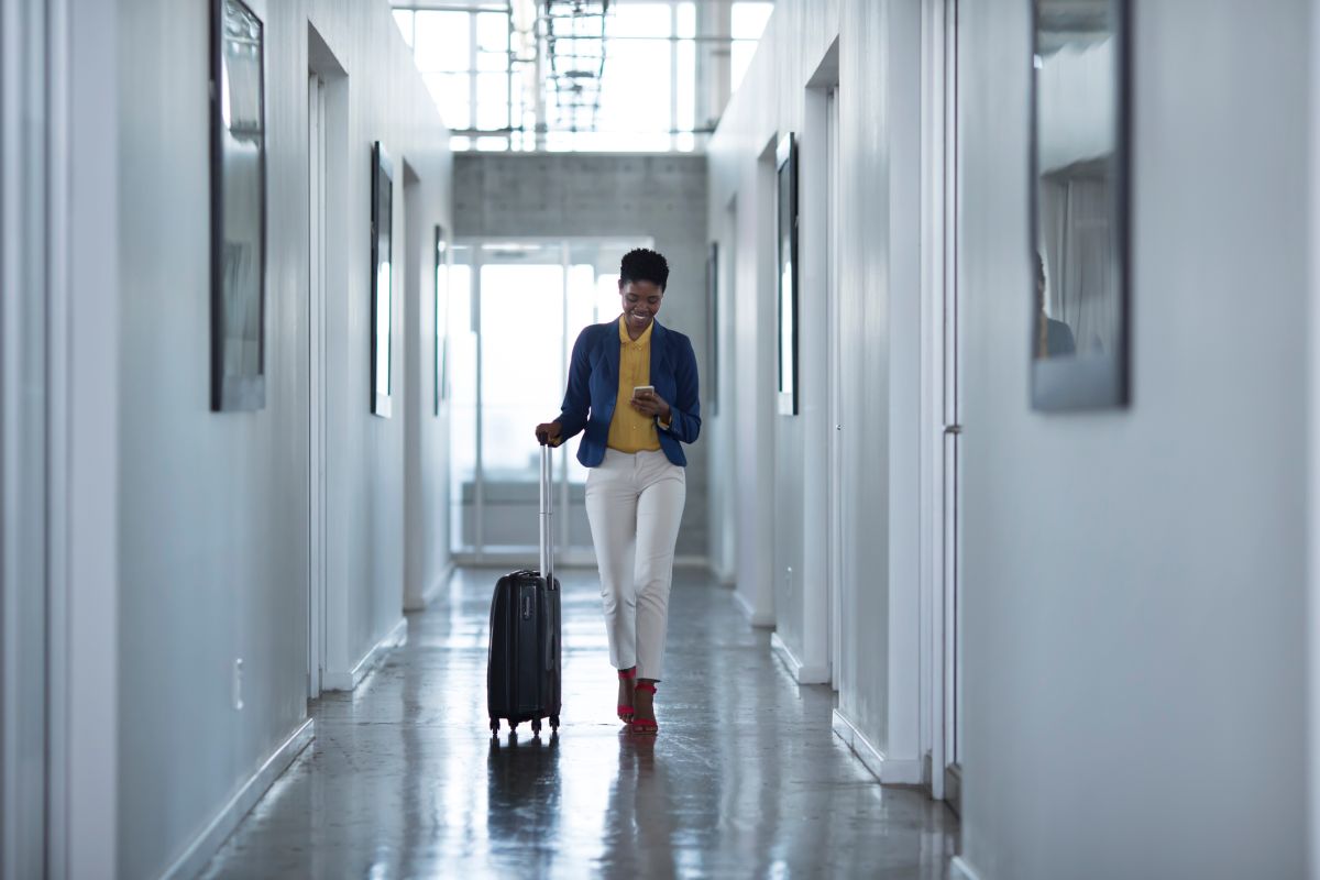 Businesswoman walking down hall way with rolling suitcase