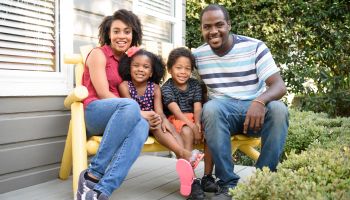 Young African American family sitting on bench outside house