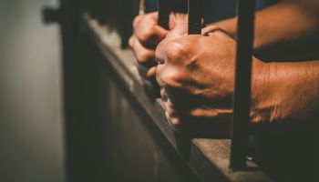 Cropped Hands Of Male Prisoner Holding Prison Bars