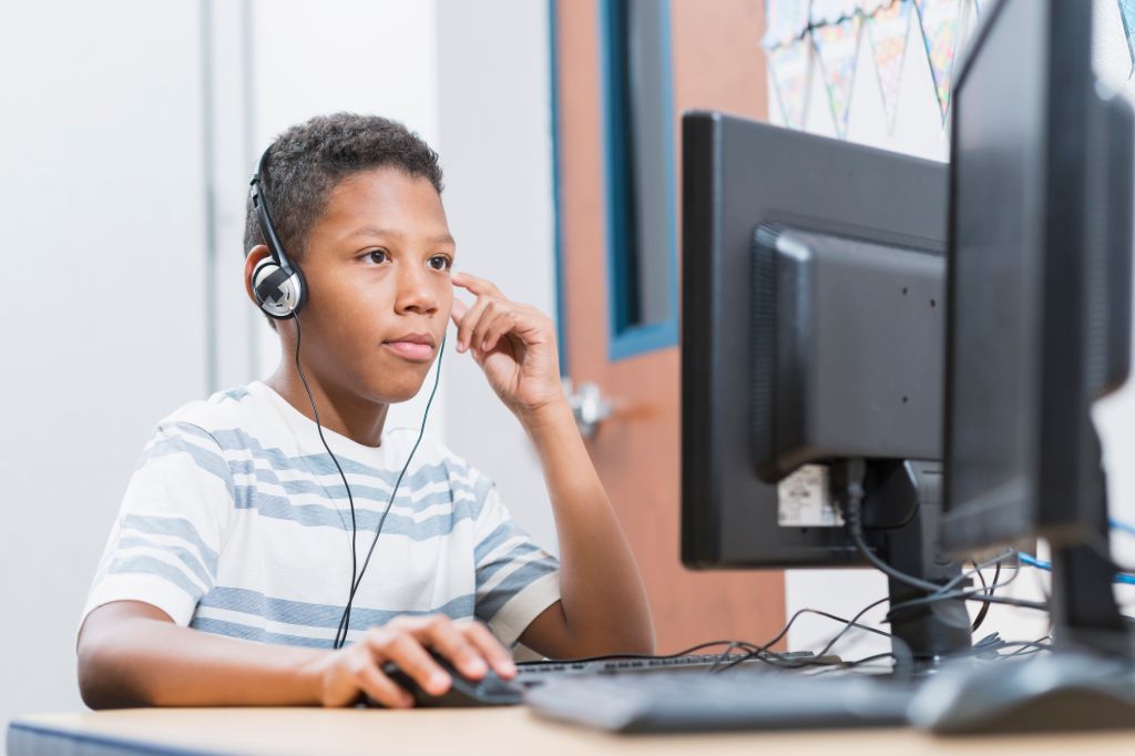 Boy in school using desktop computer wearing headphones