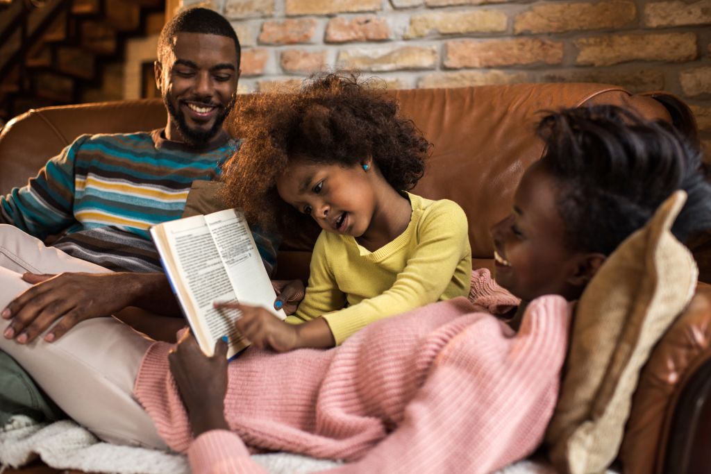 Little African American girl reading a book to her parents.