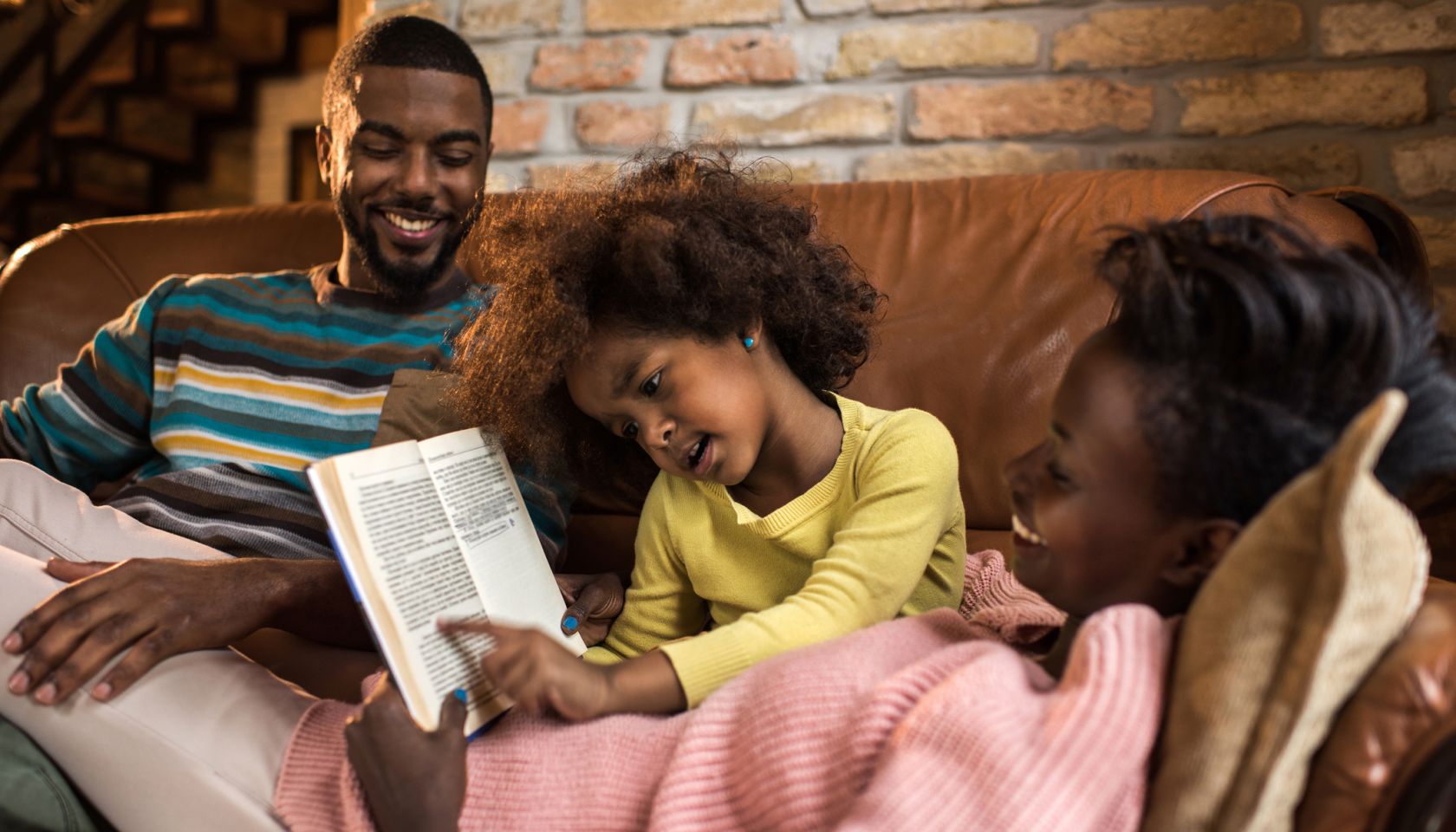 Little African American girl reading a book to her parents.
