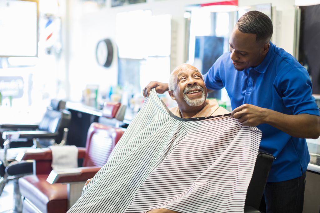 Black barber tying apron on customer in retro barbershop