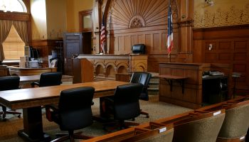 An empty, brown-paneled courtroom with flags