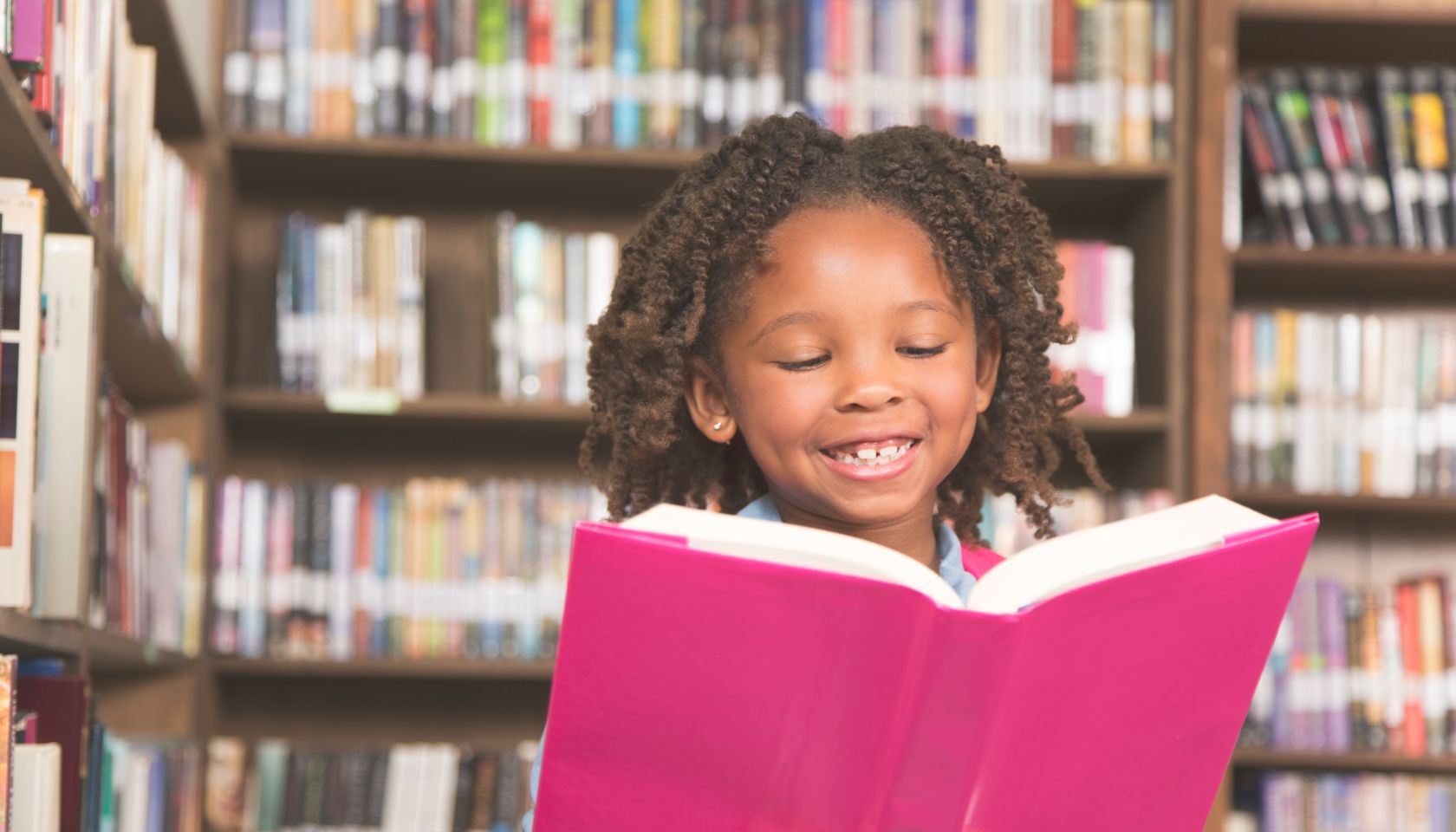 African descent little girl in school library reading book.