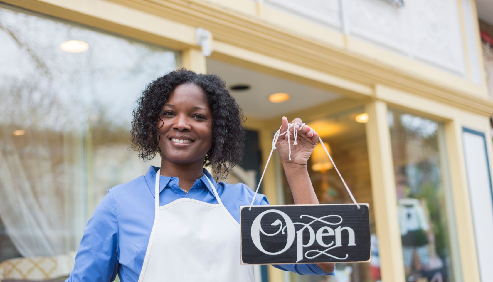 African American woman with apron holding an open sign
