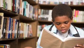 African descent boy in school library reading book.