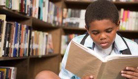 African descent boy in school library reading book.