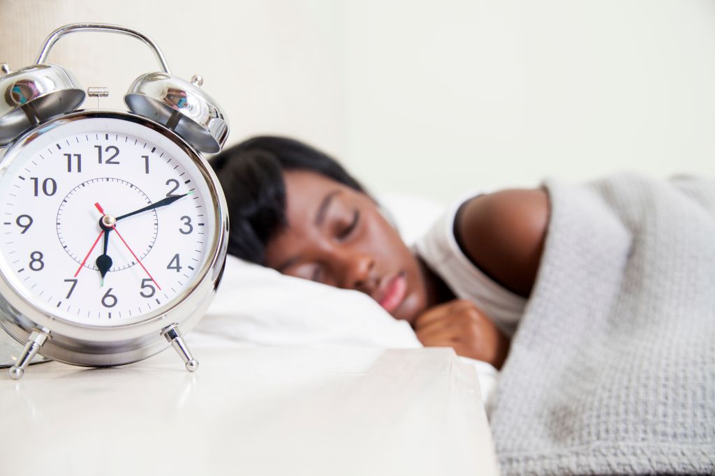 African teenaged girl sleeping, double bell alarm clock foregrounded, Cape Town, South Africa