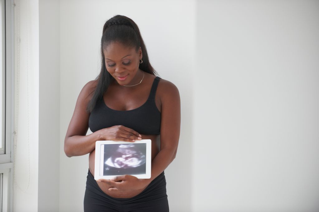 Pregnant Black woman showing sonogram on digital tablet
