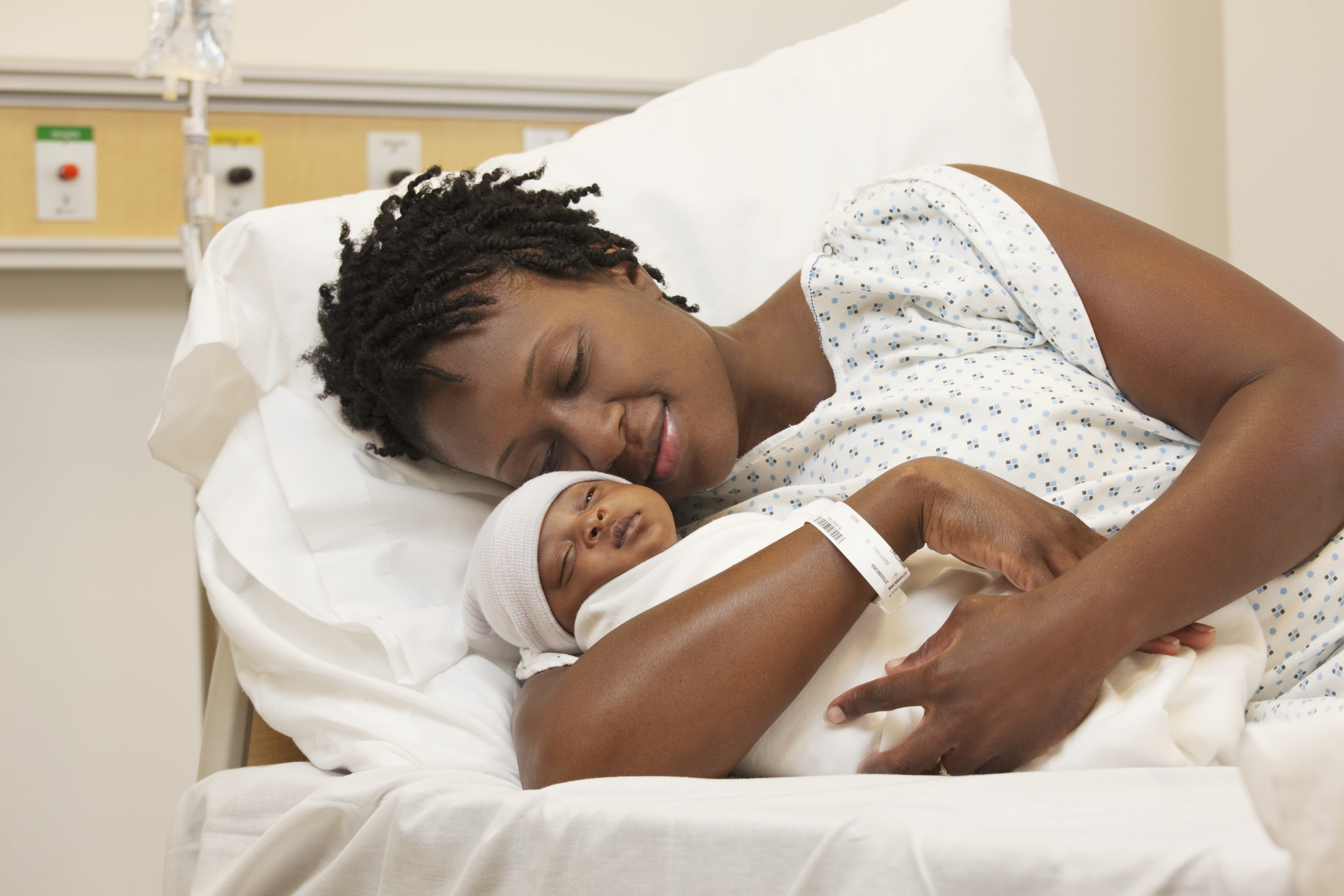 Black woman holding newborn baby in hospital bed