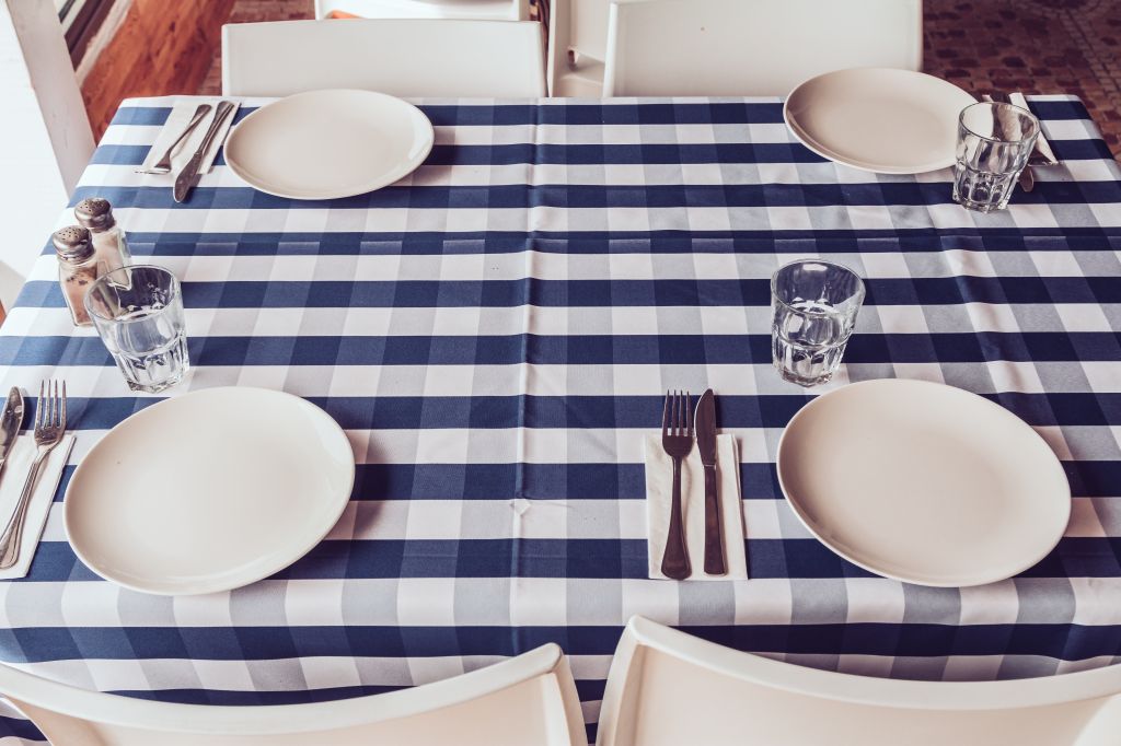 White plates, fork and knives, blue stripy tablecloth, drinking glasses