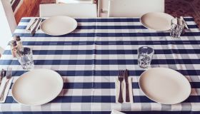 White plates, fork and knives, blue stripy tablecloth, drinking glasses