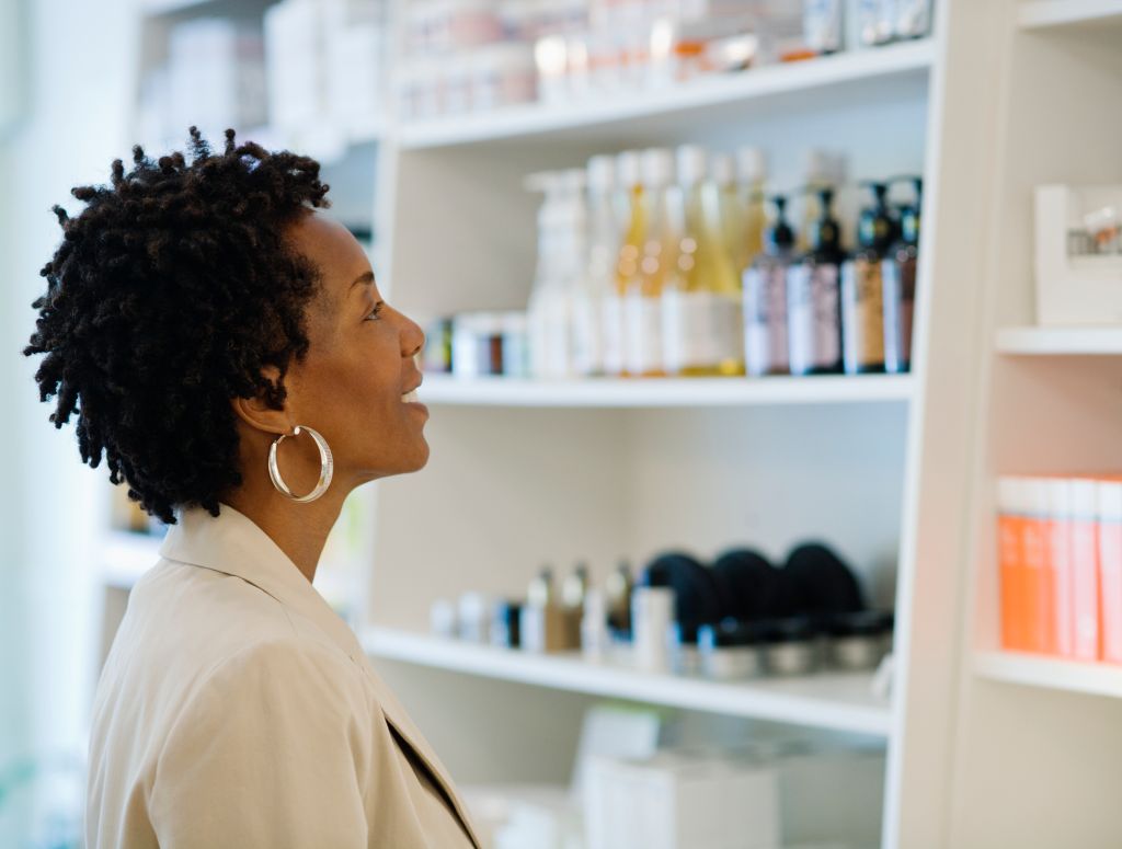 Mature woman looking at cosmetic merchandise on shelves in shop, side view