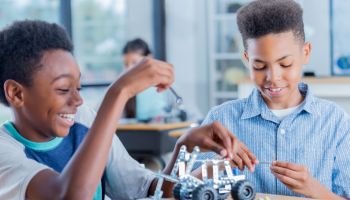 Two preteen boys work on robotics project together at school