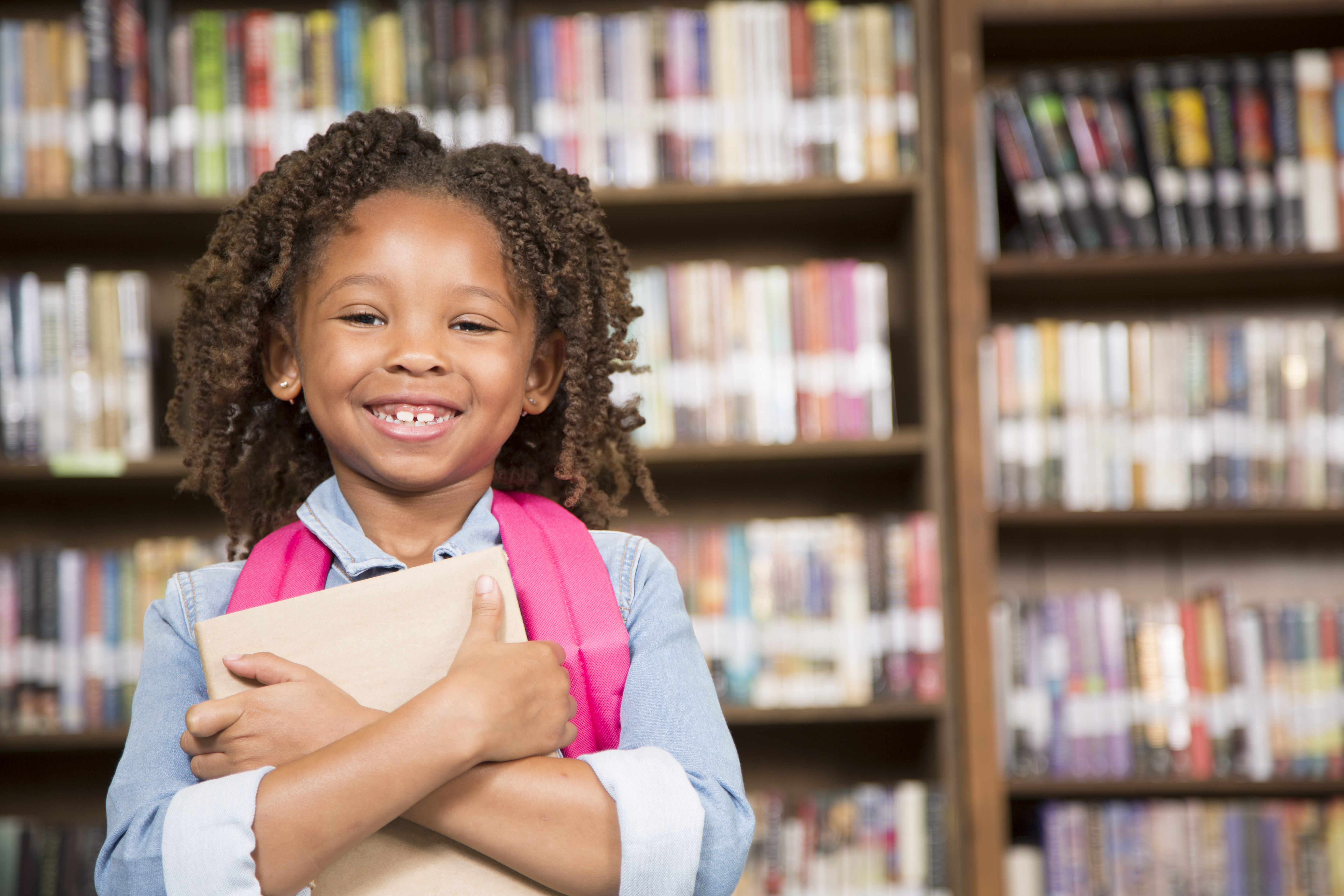 African descent little girl in school library with book.