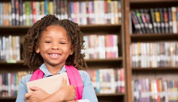 African descent little girl in school library with book.
