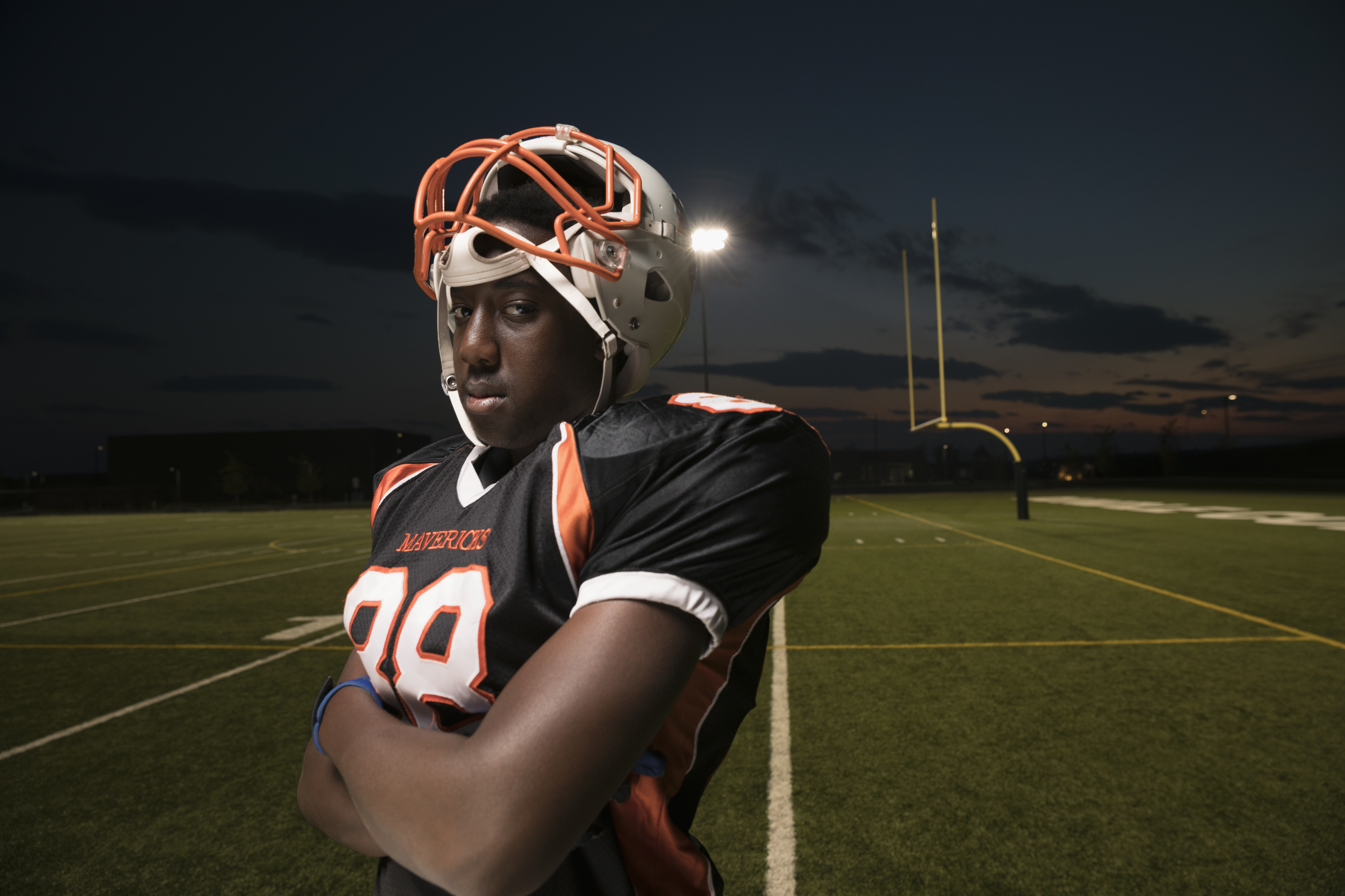 Portrait confident, tough teenage boy high school football player on football field at night