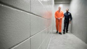 Bailiff walking prisoner in orange jumpsuit down corridor in jail